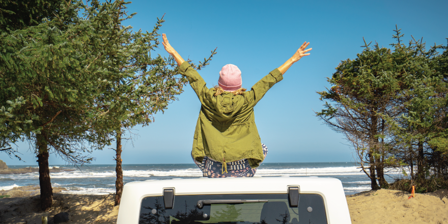 Person standing through sunroof car near coast